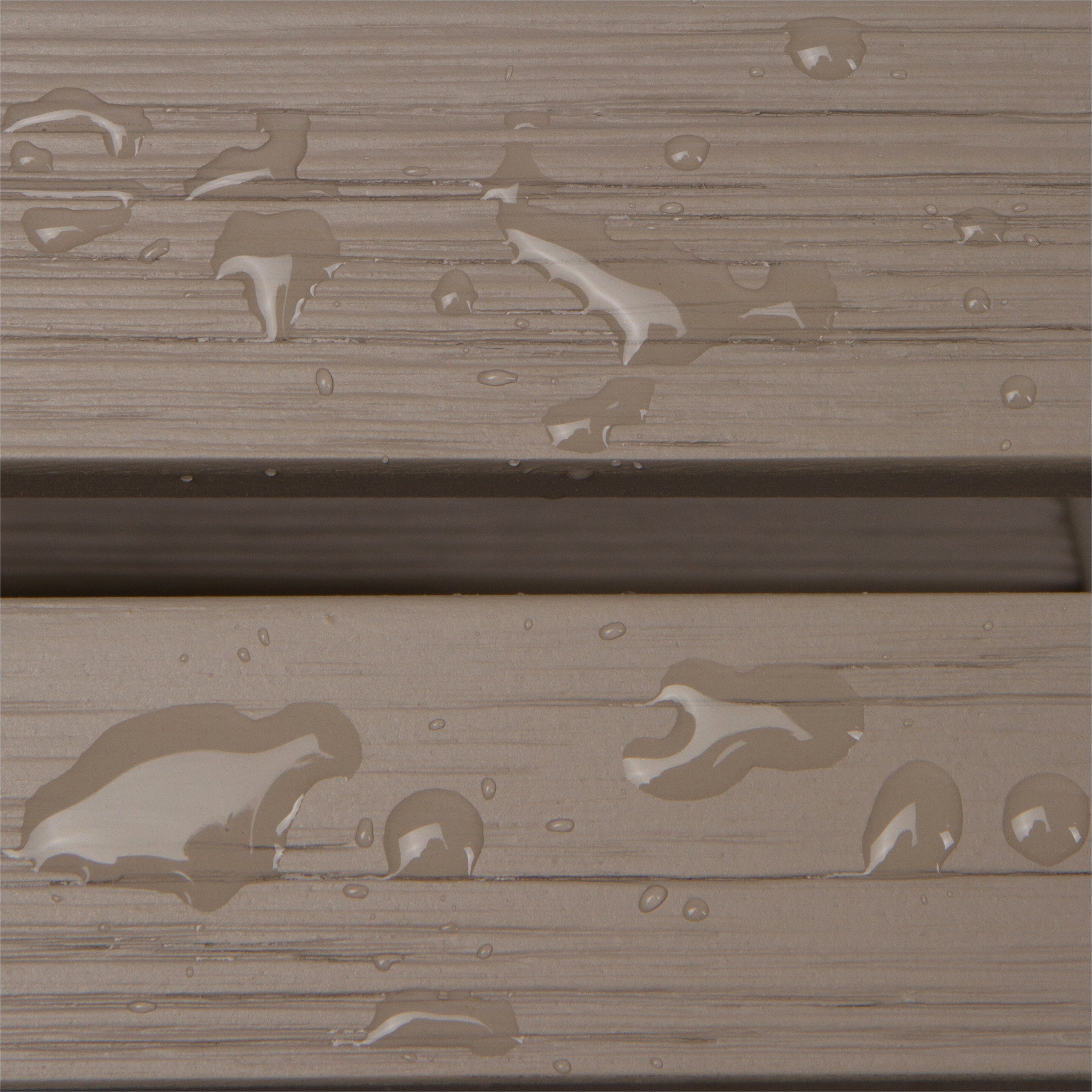 Close-up of a weathered taupe-brown wood or composite plank surface with water droplets and small puddles showing through the textured finish.