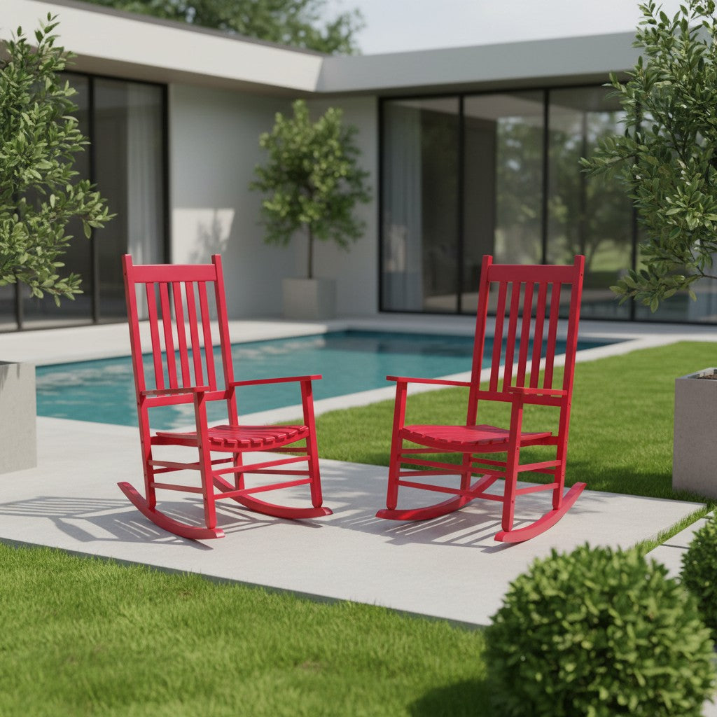 Two bright red rocking chairs placed on a concrete patio beside a swimming pool in a modern backyard setting with green grass and shrubs.