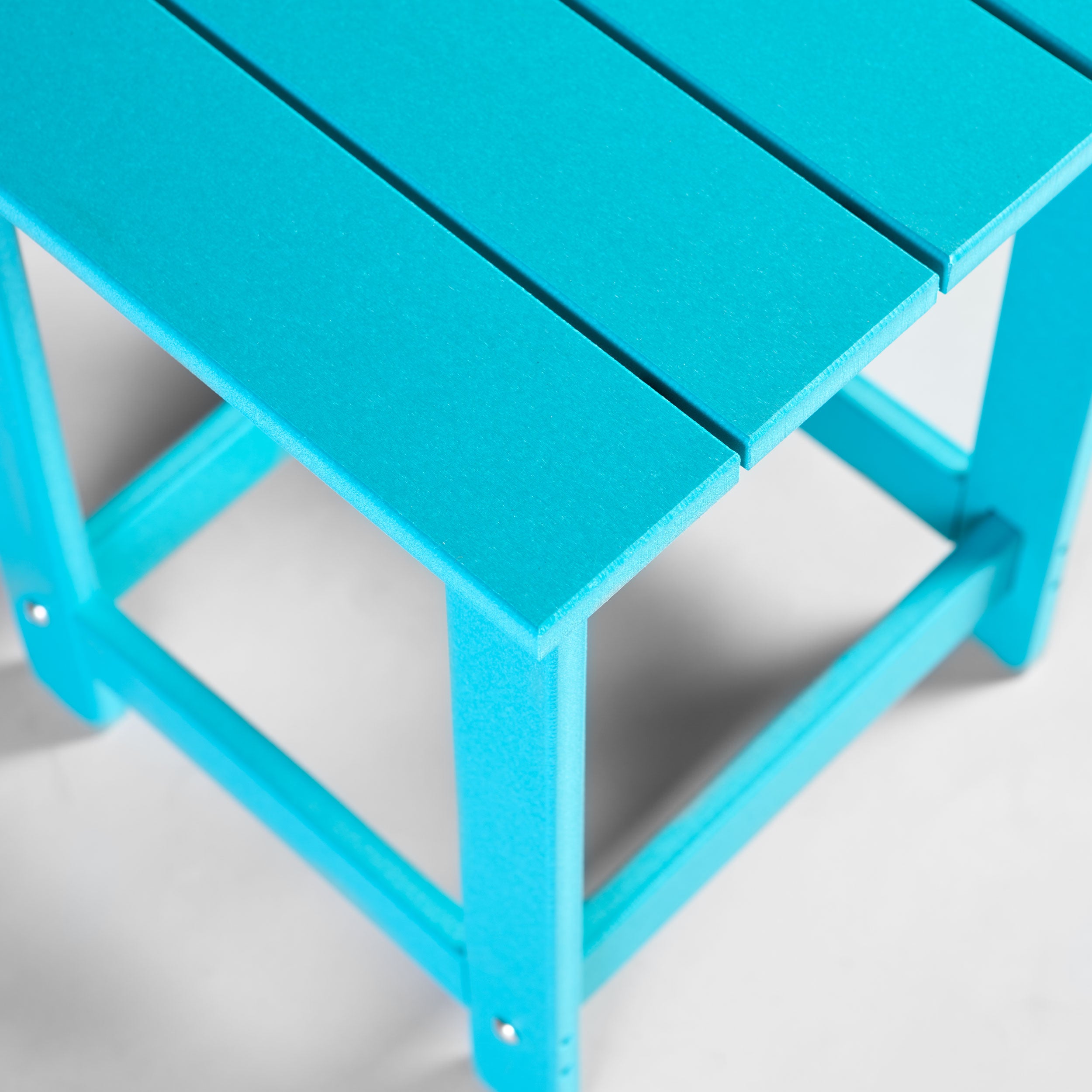 A close-up of a bright turquoise blue slatted plastic small table with a matching frame, photographed on a clean white background.