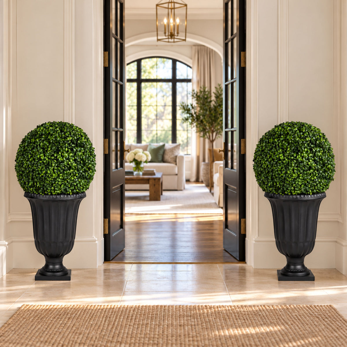 Two large black urn-shaped planter boxes with neatly trimmed round green topiary trees, placed symmetrically on either side of open dark-framed doors in an elegant interior hallway leading to a sunlit living room.