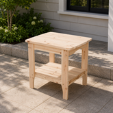 A natural cedar wood rectangular outdoor side table with a slatted top and a lower shelf, placed on a stone patio. 