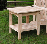 A natural cedar wood two-tier rectangular side table with a slatted top and lower shelf on a grassy lawn. 