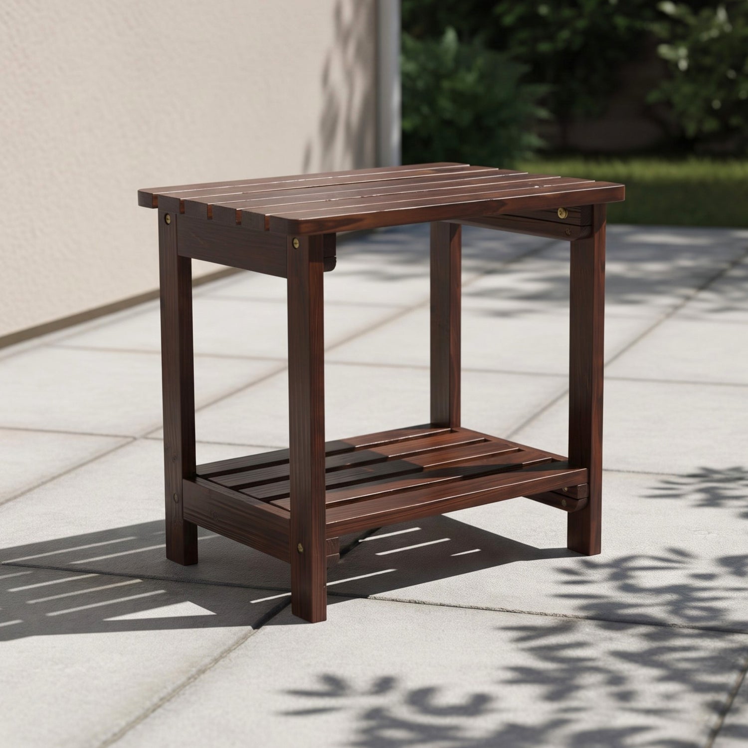 A dark brown wooden outdoor side table with a slatted top and lower shelf, shown on a light stone patio in a real outdoor setting with shadows from nearby foliage. 