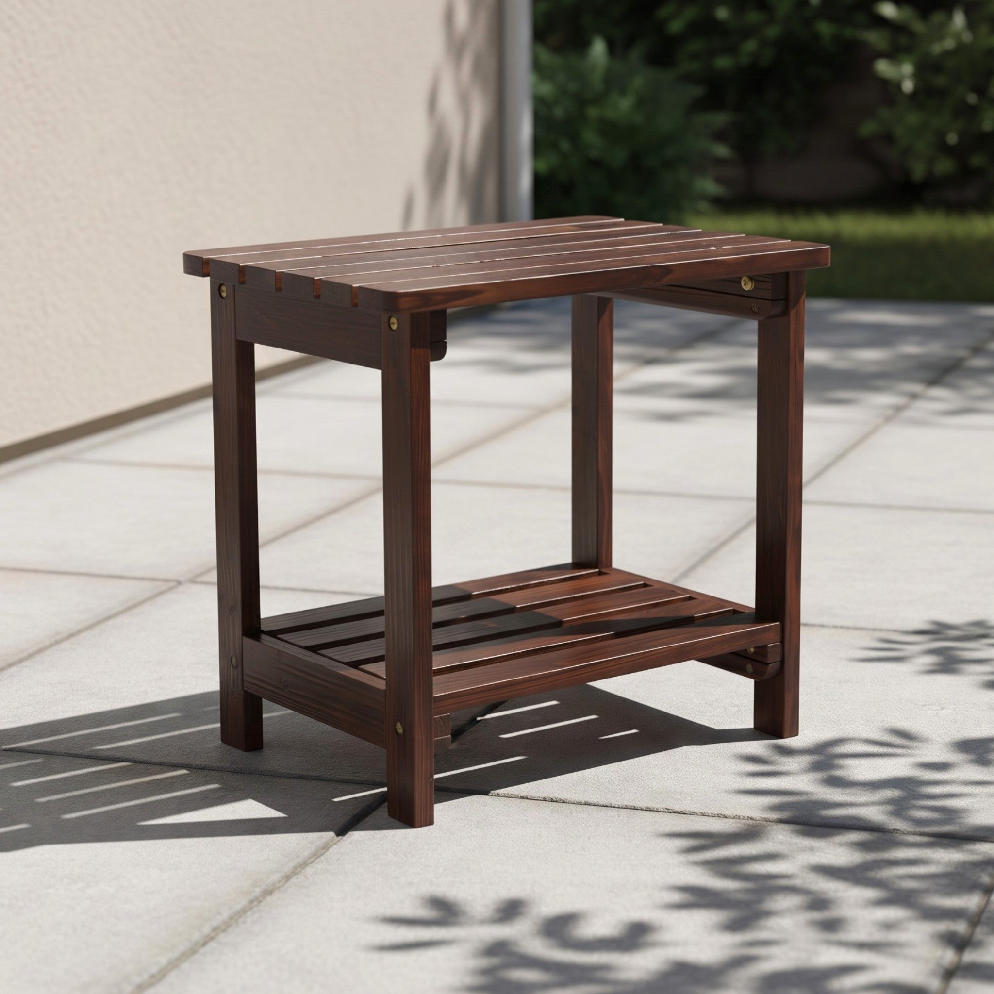 A dark brown wooden outdoor side table with a slatted top and lower shelf, shown on a light stone patio in a real outdoor setting with shadows from nearby foliage. 