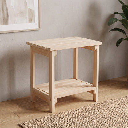 A light natural wood side table with an open lower shelf, shown in a styled room setting with a textured wall, wood floor, and a plant in the background. 