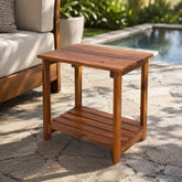 Wooden side table on a stone patio with outdoor furniture and pool in the background 