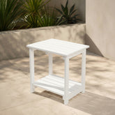 White outdoor side table on a patio with plants in the background 