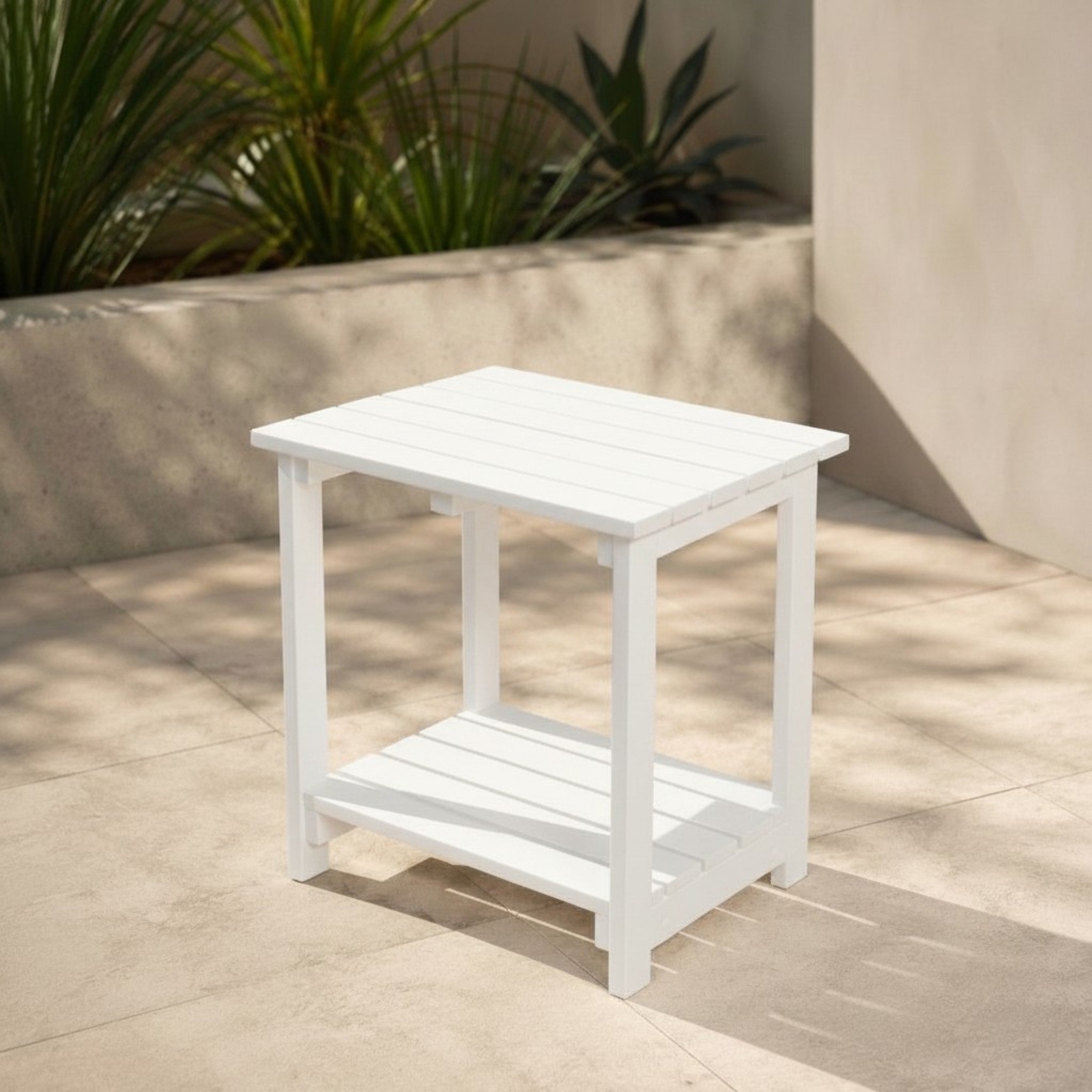 White outdoor side table on a patio with plants in the background 