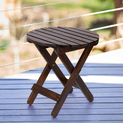 A round folding wooden side table with a dark brown slatted top and X-frame legs, shown on a blue deck with a blurred outdoor background. 