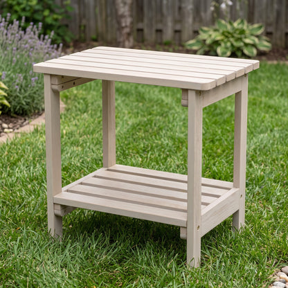 A light beige outdoor wooden end table with a slatted top and lower shelf, shown on a green lawn in a backyard setting. 