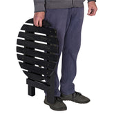 A person holding a black folding slatted bench or chair against a plain white background. 