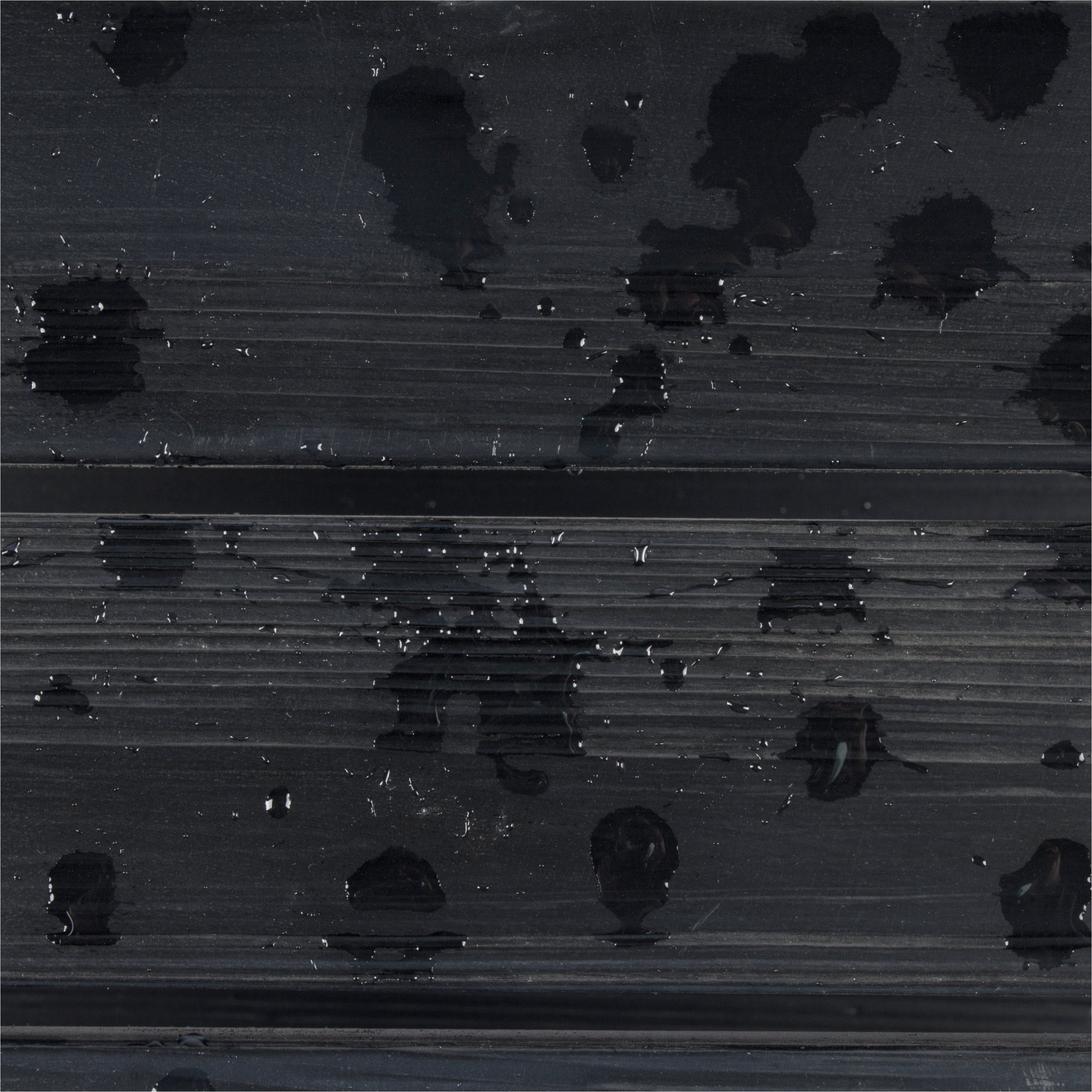 A close-up of a dark charcoal gray ribbed surface with glossy black water droplets and small reflective highlights. 