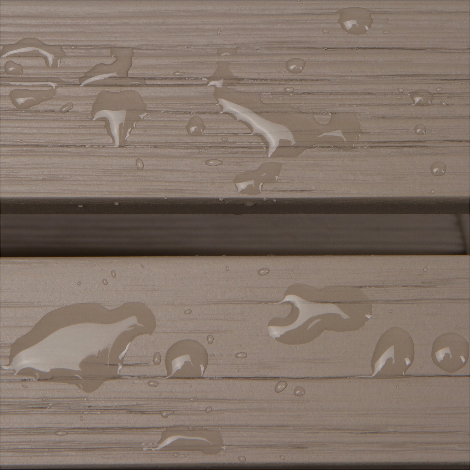 Close-up of a weathered taupe-brown wood or composite plank surface with water droplets and small puddles showing through the textured finish. 
