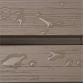 Close-up of a weathered taupe-brown wood or composite plank surface with water droplets and small puddles showing through the textured finish. 