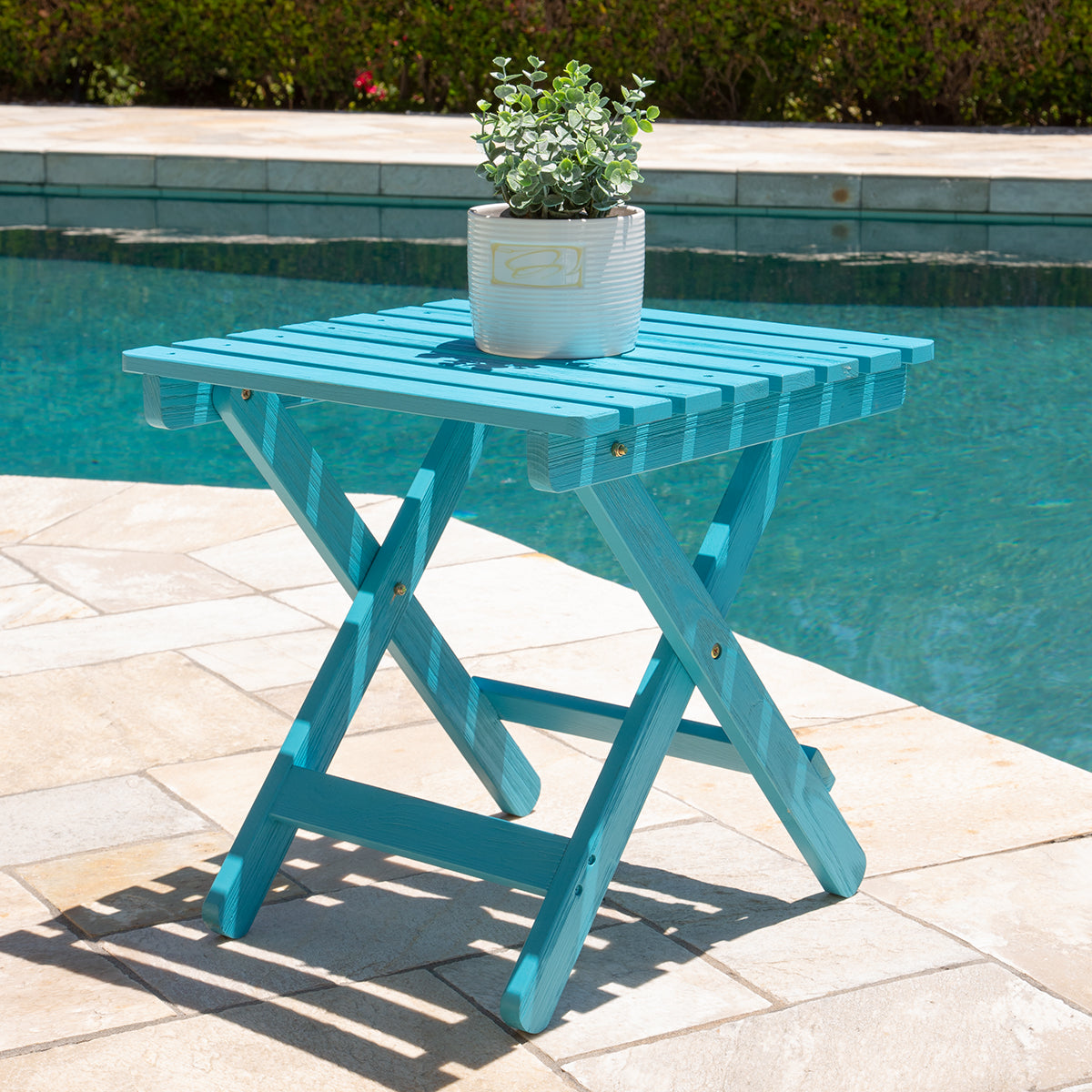 Blue folding table with a plant on it by a pool 