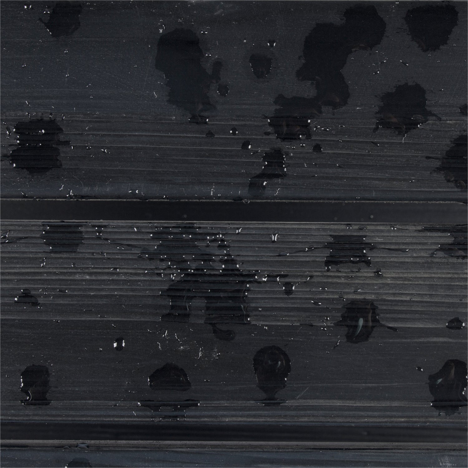 A close-up of a dark charcoal gray ribbed surface with glossy black water droplets and small reflective highlights. 