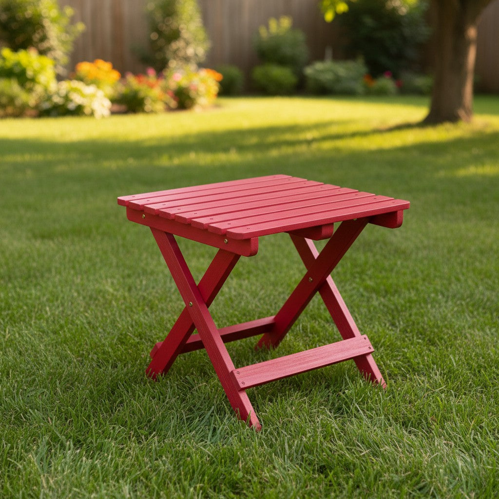 A small red folding side table made of slatted wood, set on a green grassy lawn in a backyard with a wooden fence and trees in the background. 