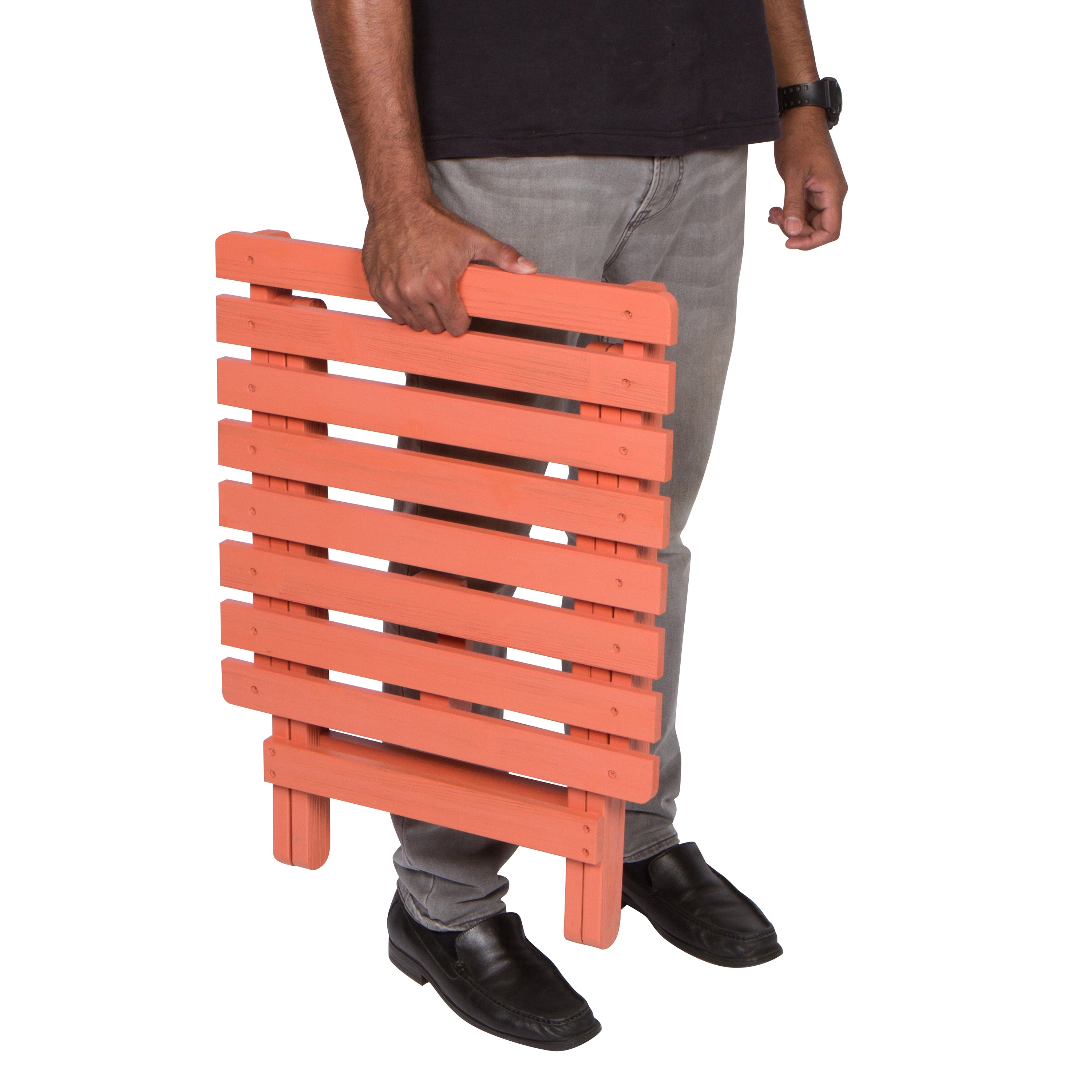A person holding a portable folding wooden side table with orange-painted slats, shown from the waist down against a plain white background. 