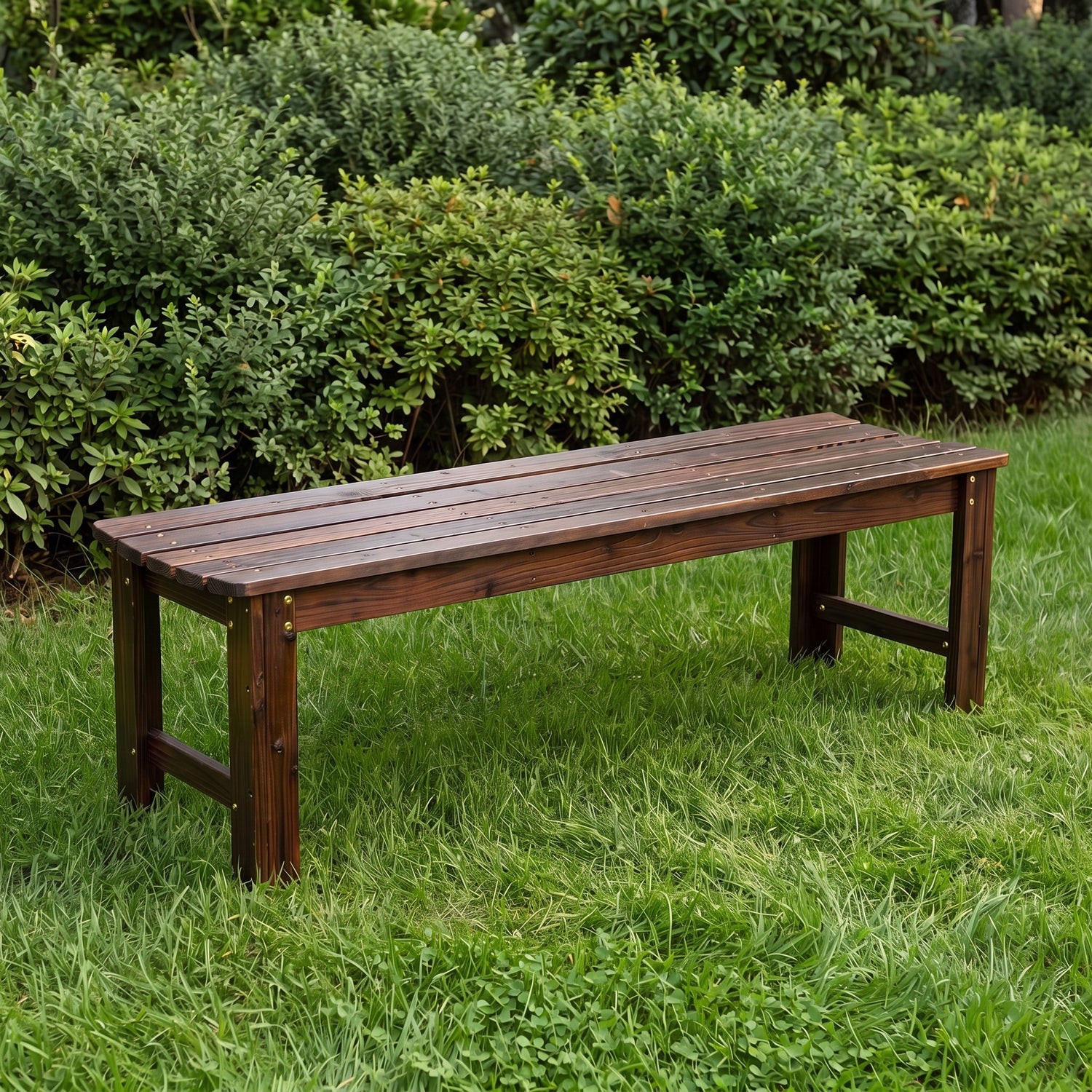 A dark brown wooden garden bench with a slatted seat and solid legs, placed on a green lawn with dense green bushes in the background. 
