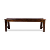 A dark brown wooden bench with a slatted seat and trestle-style legs, shown from the side against a plain white background. 