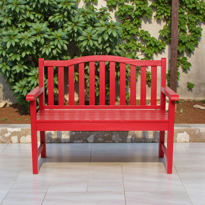 A bright red wooden garden bench with armrests and vertical slats, positioned on a light tiled patio in front of a stone wall and green ivy. 