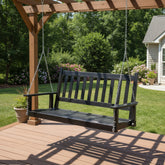 A black wooden porch swing hanging from chains under a brown wooden pergola on a deck, with a green backyard and house visible in the background. 