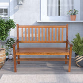 A wooden outdoor bench with a slatted back and seat, shown in a patio setting with potted plants and a gray stucco wall background. 