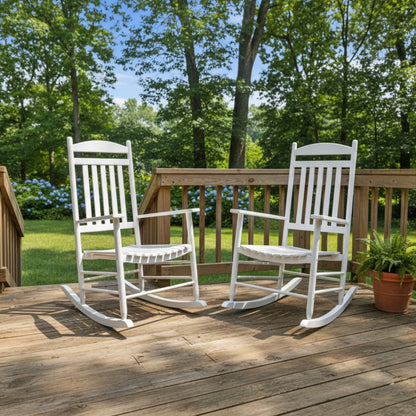 Two white wooden rocking chairs on a wooden deck with a green lawn and trees in the background. 
