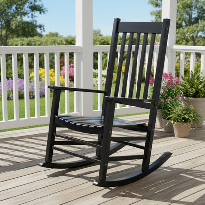 A black rocking chair on a wooden deck with a white railing and garden plants in the background. 