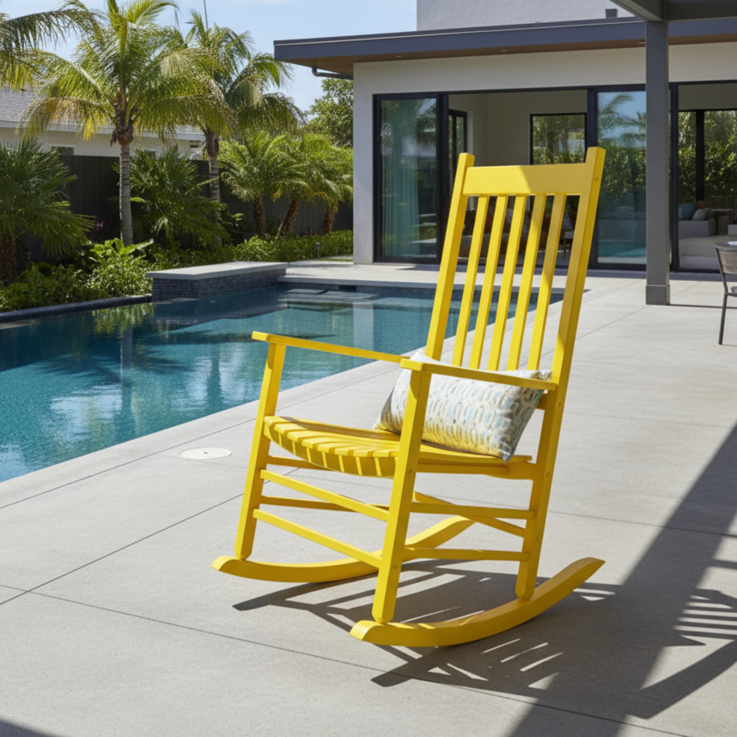 Yellow rocking chair with a cushion on a patio by a poolside. 