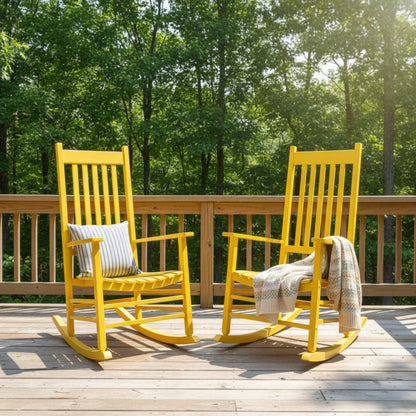 Two bright yellow outdoor rocking chairs on a wooden deck with a green forest background. One chair has a striped pillow, and the other has a beige throw blanket. 