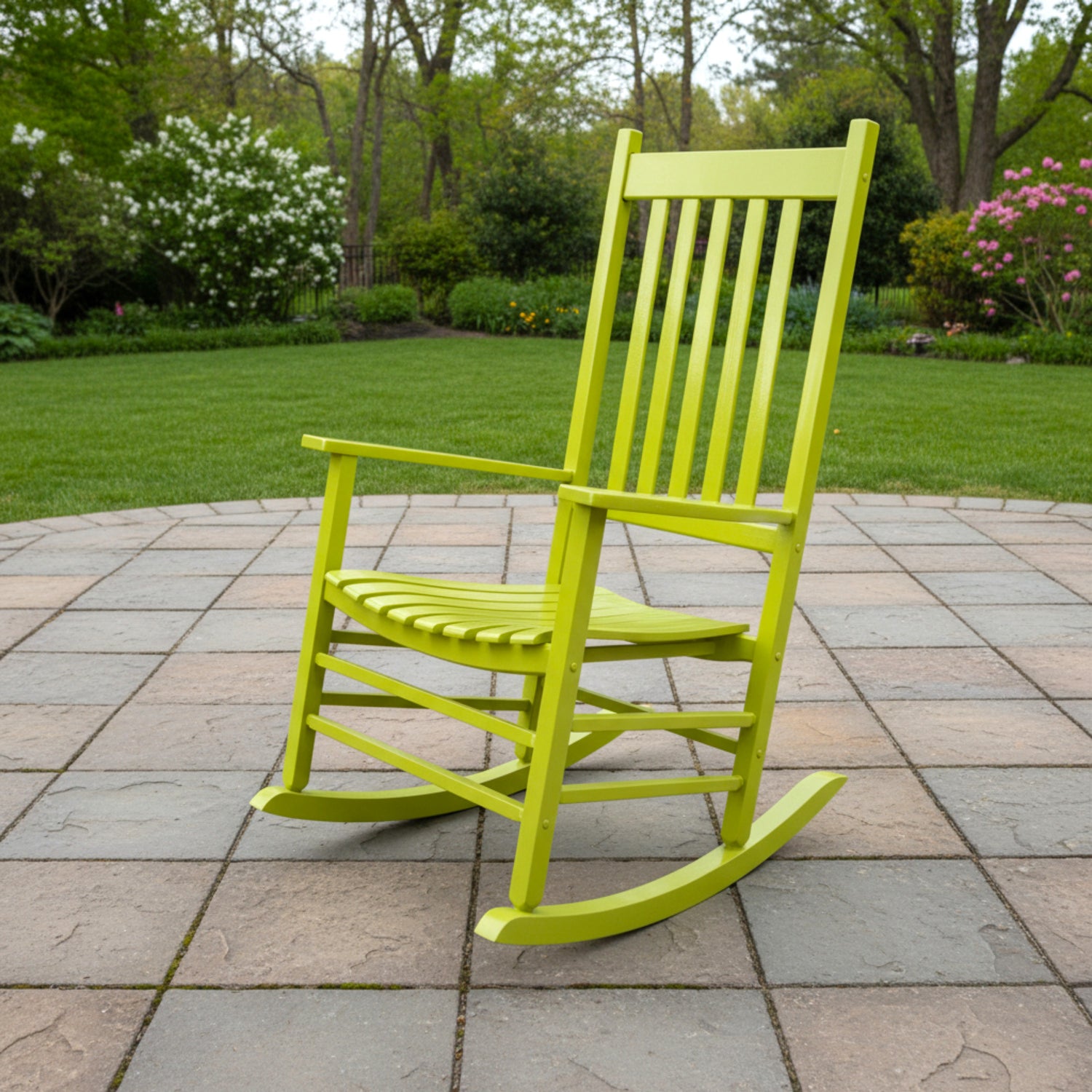 A bright lime green wooden rocking chair positioned on a stone patio with a green lawn and trees in the background. 