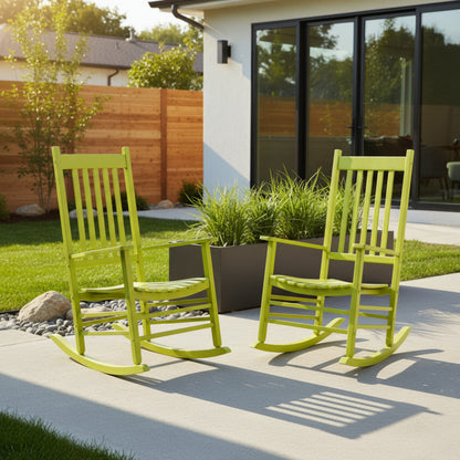 Two bright lime green outdoor rocking chairs placed on a concrete patio in front of a modern house with large black-framed glass windows, grass, shrubs, and a wooden fence. 