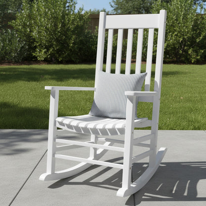 A white outdoor rocking chair with a gray striped throw pillow, set on a concrete patio with a green lawn and trees in the background. 