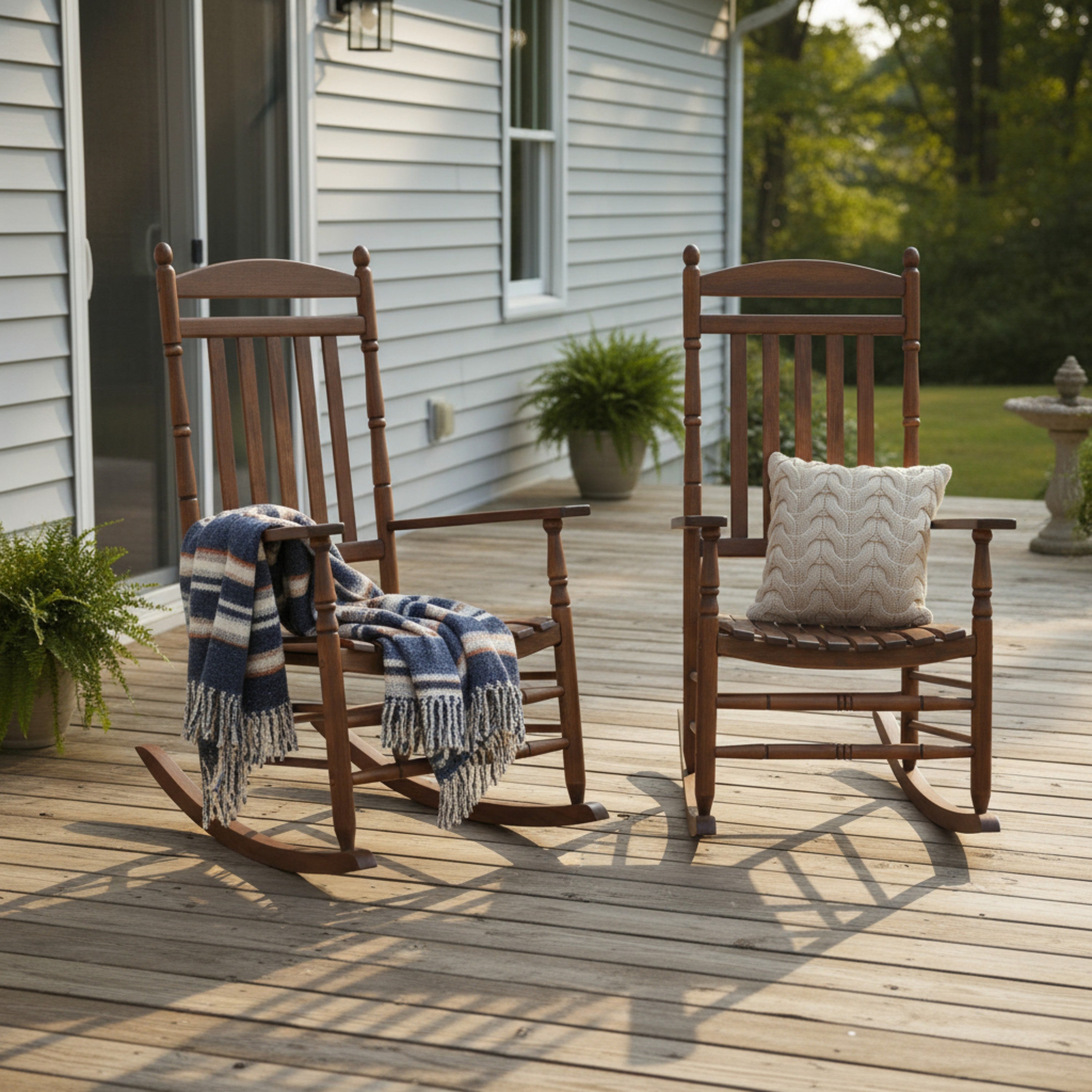 Two wooden rocking chairs on a deck outside a house. One chair has a blue, white, and navy striped throw blanket draped over it, and the other has a white textured pillow. 