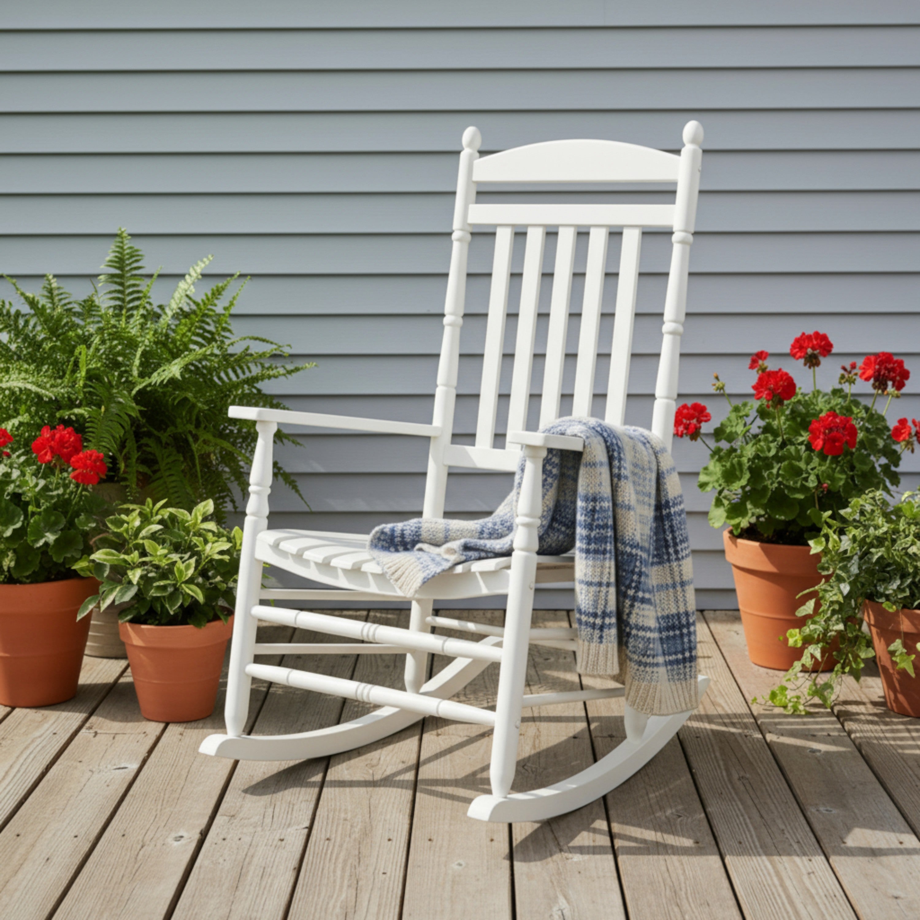 White rocking chair on a wooden deck with potted plants and flowers. 