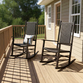 Two outdoor rocking chairs on a wooden deck next to a house, with one chair featuring a striped pillow. 
