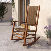 A wooden rocking chair with woven wicker-style seat and back slats, shown outdoors on a patio beside a stucco wall, glass door, and potted lavender plants. 