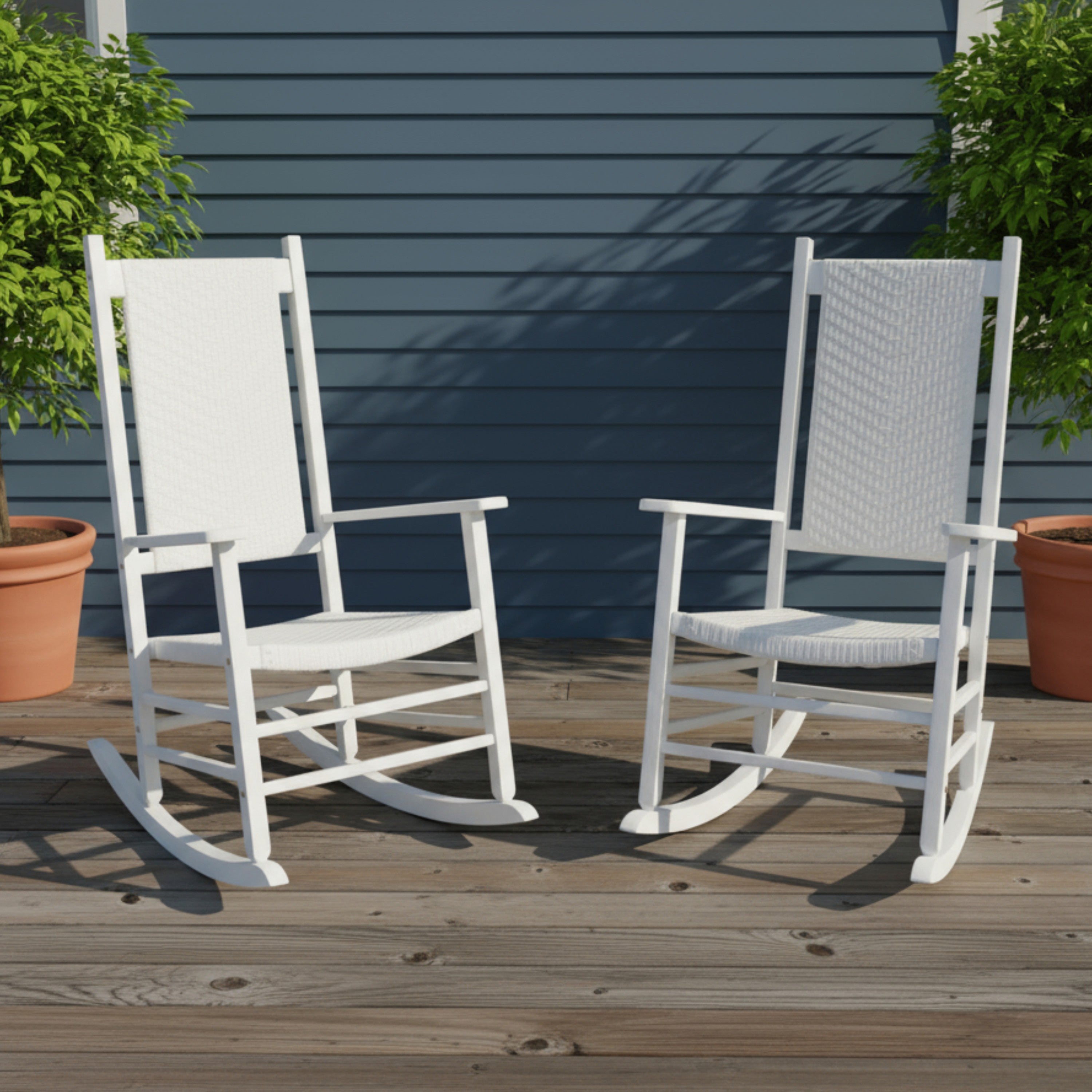 Two white outdoor rocking chairs with woven sling backs and seats, placed on a wooden deck in front of a blue house siding wall with potted plants on either side. 