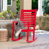 A bright red outdoor rocking chair on a covered patio with a gray throw blanket draped over the seat. The chair is positioned next to a woven side table, with stone columns, plants, and a tiled wall in the background. 