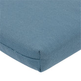 Close-up of a textured blue woven fabric cushion corner with a visible seam on a white background. 