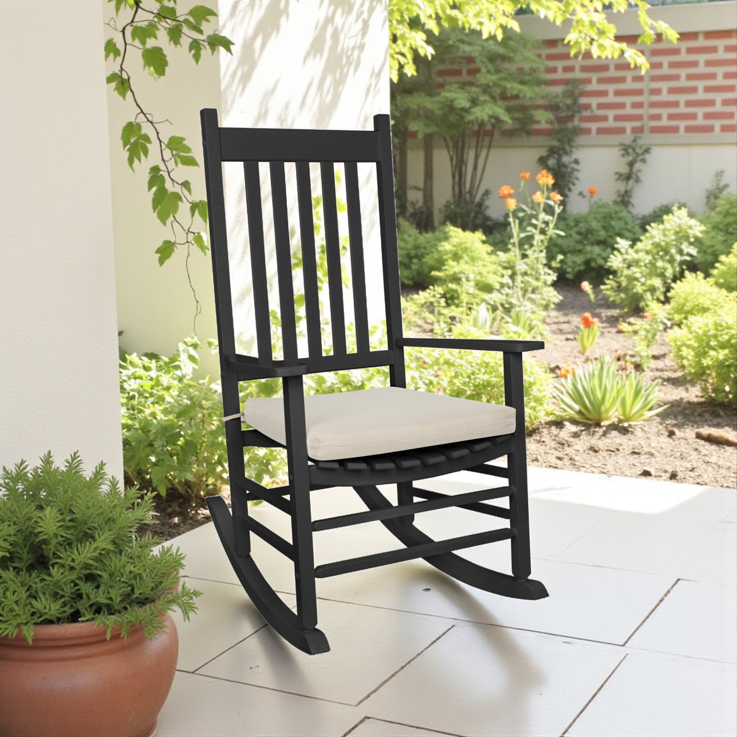 A black rocking chair with a light khaki  cushion sits on a tiled porch in a garden setting 
