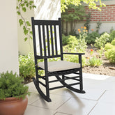 A black rocking chair with a light khaki  cushion sits on a tiled porch in a garden setting 