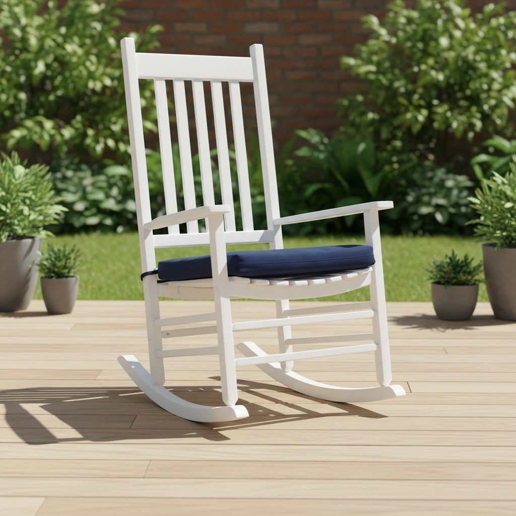 A white wooden rocking chair with a navy blue cushioned seat and backrest, set on a light wood deck with a green garden and brick wall background. 
