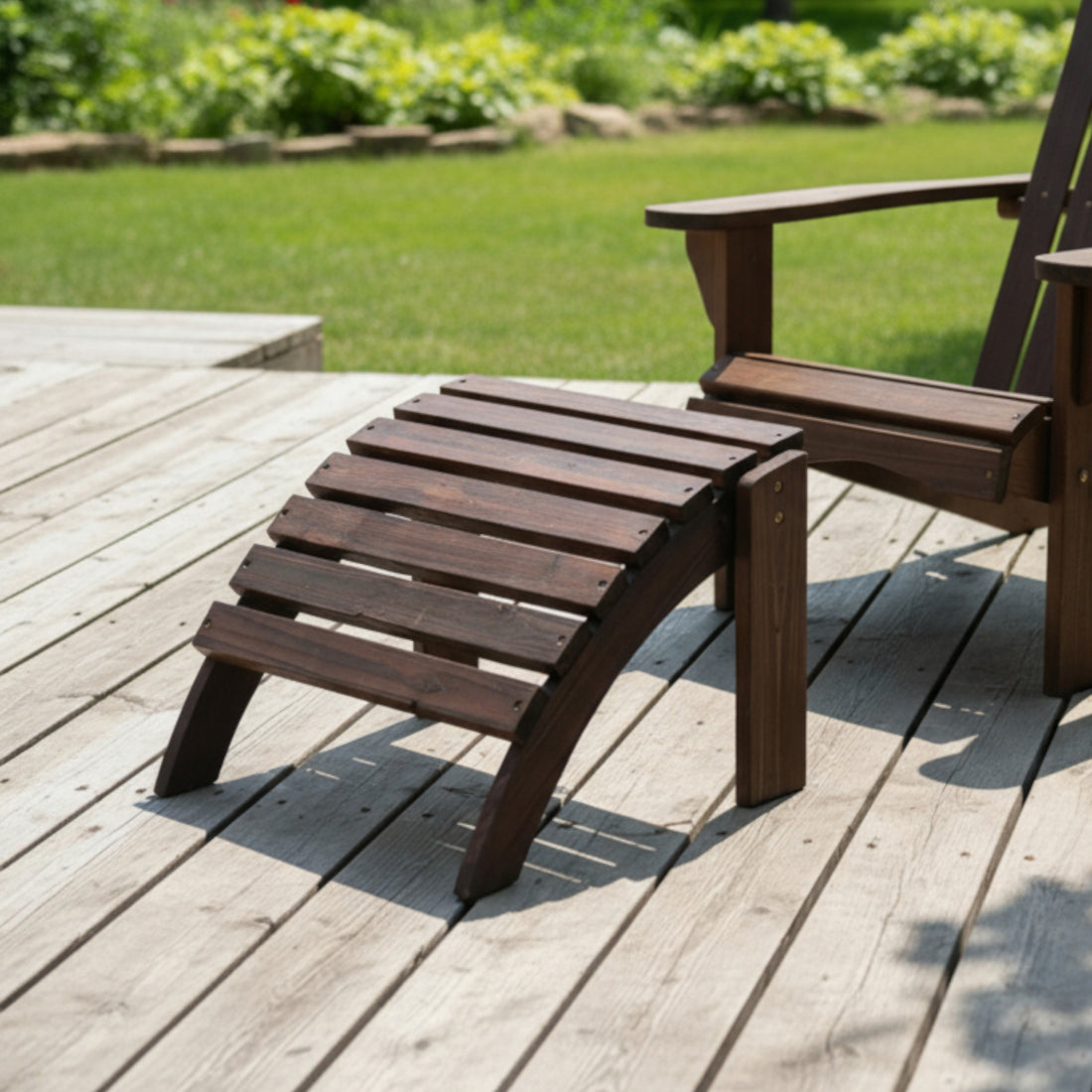 A dark brown wooden outdoor lounge chair and matching footrest set on a light gray wooden deck with a green lawn in the background. 