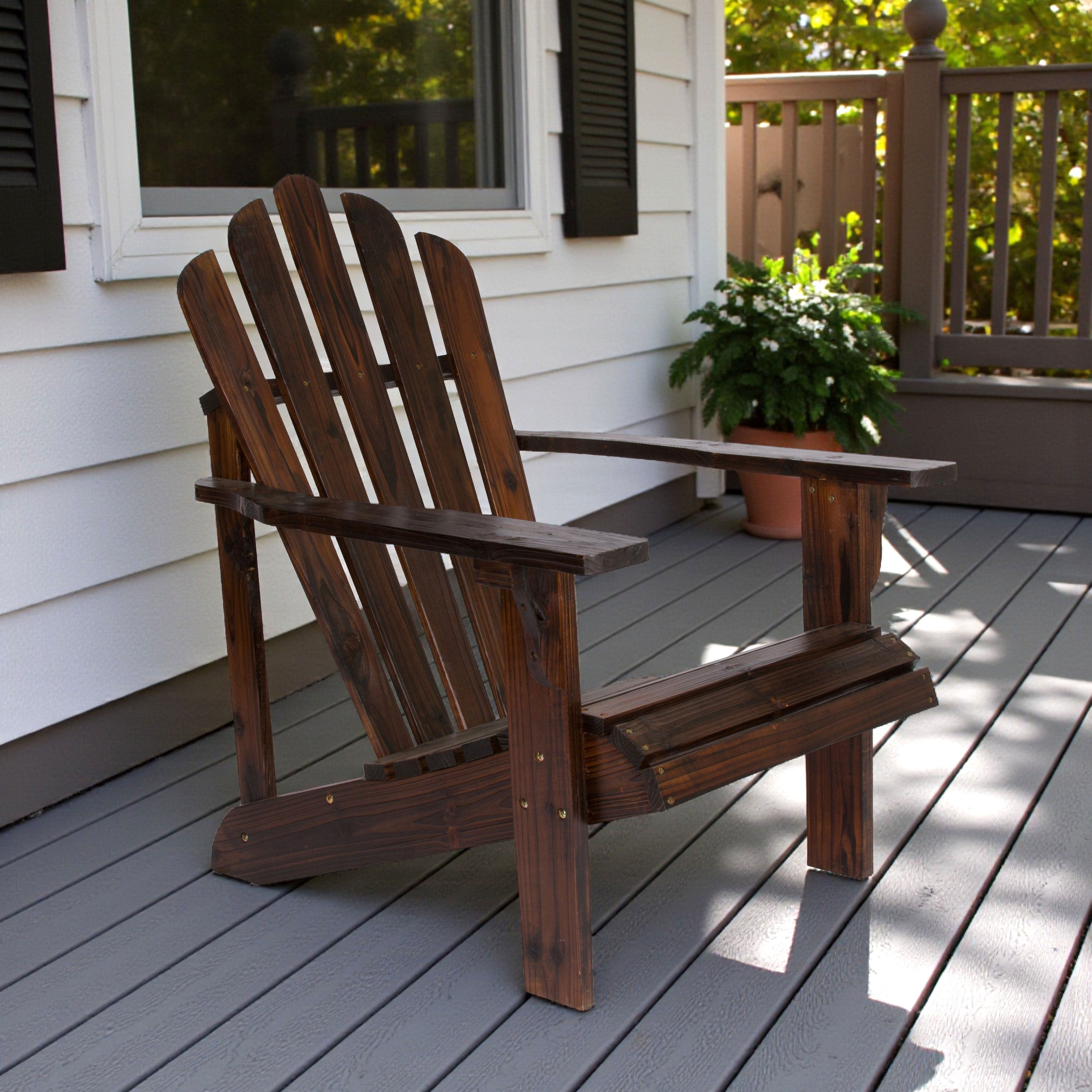 Wooden Adirondack chair on a deck with a house and plants in the background. 