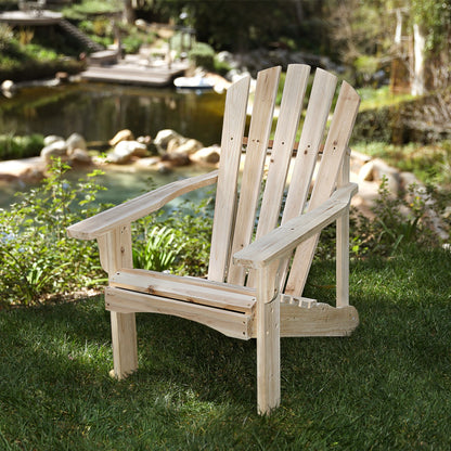 A light natural wood Adirondack chair placed on green grass in a backyard garden setting with a pond and rocks in the background. 