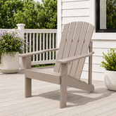 A light grayish-brown outdoor Adirondack chair on a wooden deck next to a white house, with potted plants and a white railing in the background. 