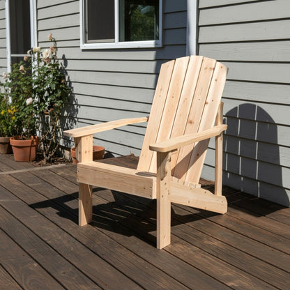 A light natural wood Adirondack chair placed on a dark wooden deck in front of a gray house exterior with potted plants visible on the left. 
