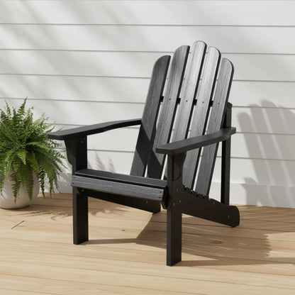 A black outdoor Adirondack chair with a slatted back and wide armrests, shown on a light wood deck against a white siding wall with a potted fern nearby. 
